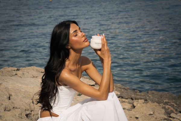 Woman with long dark hair holding Hadrill The Treatment Mask beside the sea
